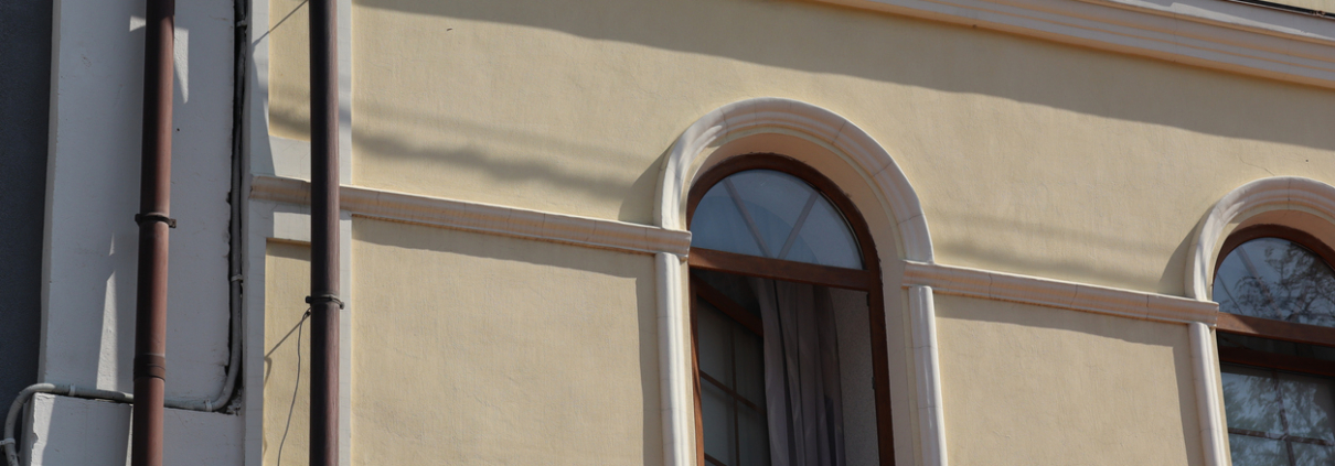 Building facade showcasing yellow exterior and arched window details captured in daylight at a cozy urban location Rendered arch and sweep moulding over a window opening